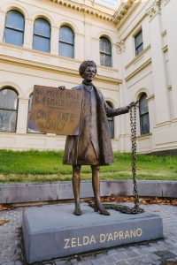 A Bronze statue of a woman holding a protest sign in one hand and a chain in the other