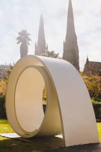 A Large Scroll Sculpture with a Church Spire and Palm Tree in the Background