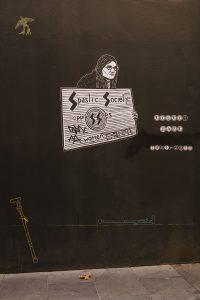 Picture of a Mural on a wall it is of A with long hair holding a protest sign
