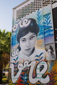 A colourful mural of a young woman with dark hair on the corner of a building