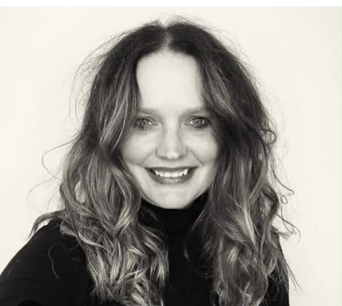 A black and white selfie of a smiling woman with long hair.