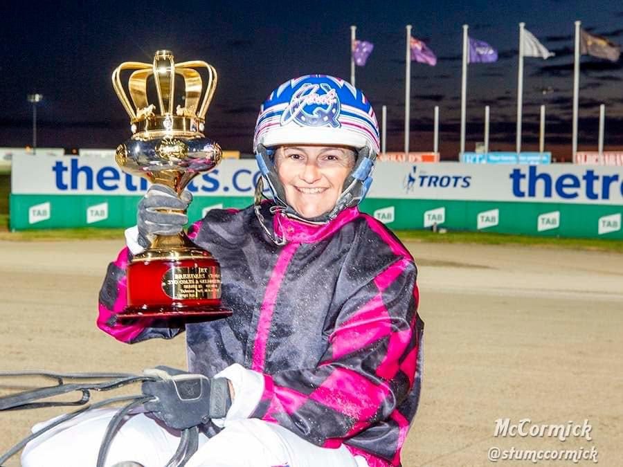A woman on horseback triumphantly holds up a trophy.