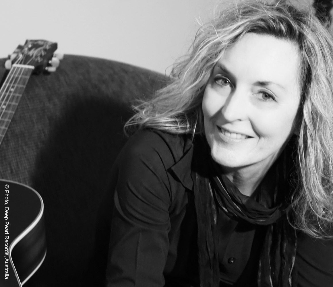 Black and white photograph of a woman smiling, with an acoustic guitar slightly out of frame to her side.