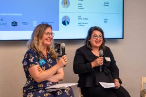 Two smiling individuals, both holding microphones near their faces. 