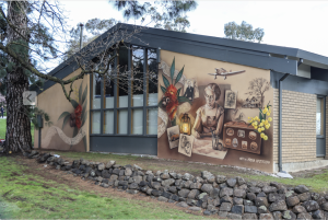 A mural of a woman at a desk surrounded by flowers, sketches and travel photos.
