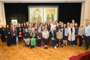 A large group of people sit and stand proudly in front of portraits of a woman
